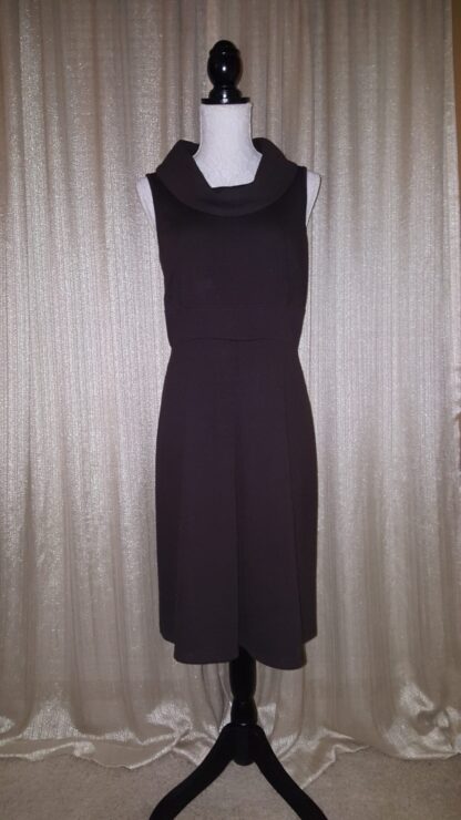 A black dress is hanging up in front of a curtain.