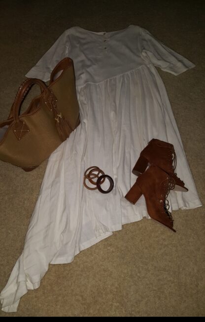 A white dress and brown purse on the floor.